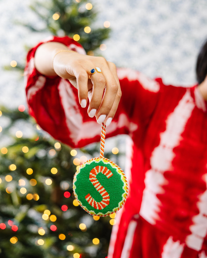 Person holding a Christmas ornament with a candy cane design in front of a decorated tree.