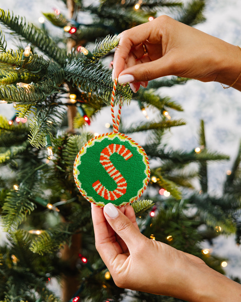 Hand holding a Christmas ornament with a candy cane design against a decorated tree background