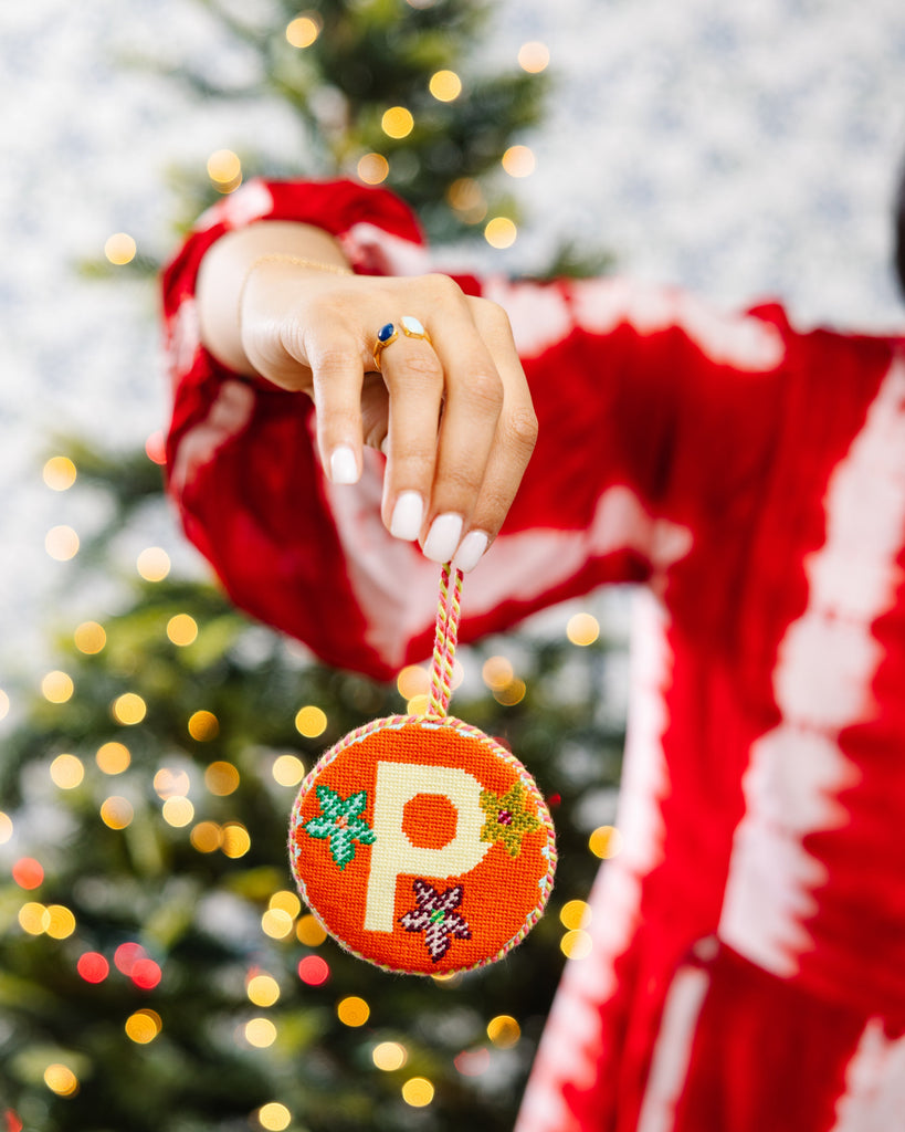 Person holding a Christmas ornament with a 'P' in front of a decorated tree
