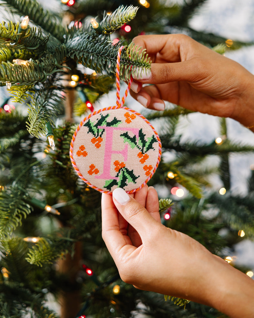 Hand holding a embroidered Christmas ornament with a tree in the background