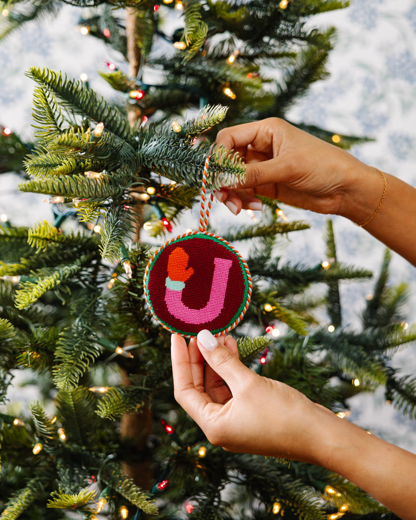 Person hanging a decorative ornament with a heart and letter 'J' on a Christmas tree.