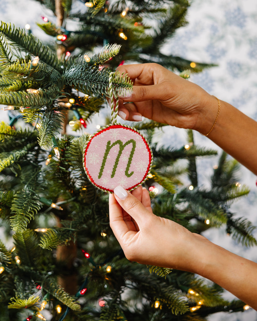 Person decorating a Christmas tree with a ornament featuring the letter 'm'.