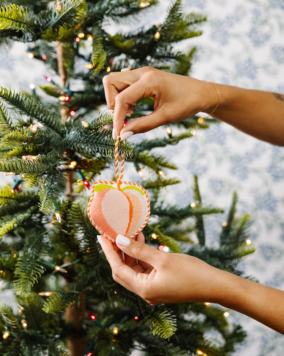 Hand placing a decorative ornament on a Christmas tree with a snowy background