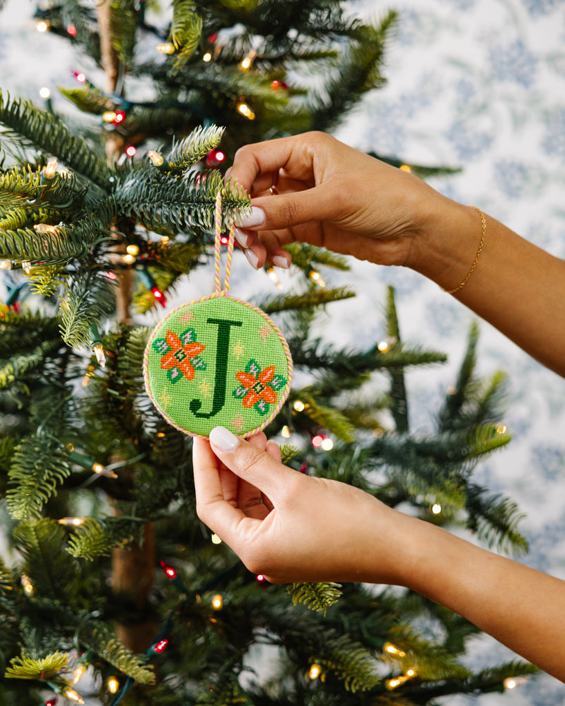 Person holding a Christmas ornament with a letter 'J' in front of a decorated tree.