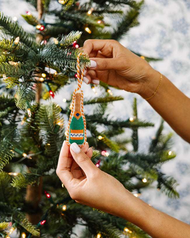 Person holding a green and orange ornament in front of a decorated Christmas tree.