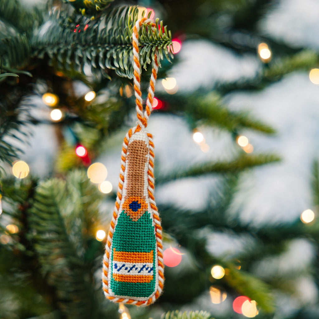 Decorative ornament shaped like a champagne bottle on a Christmas tree with lights in the background