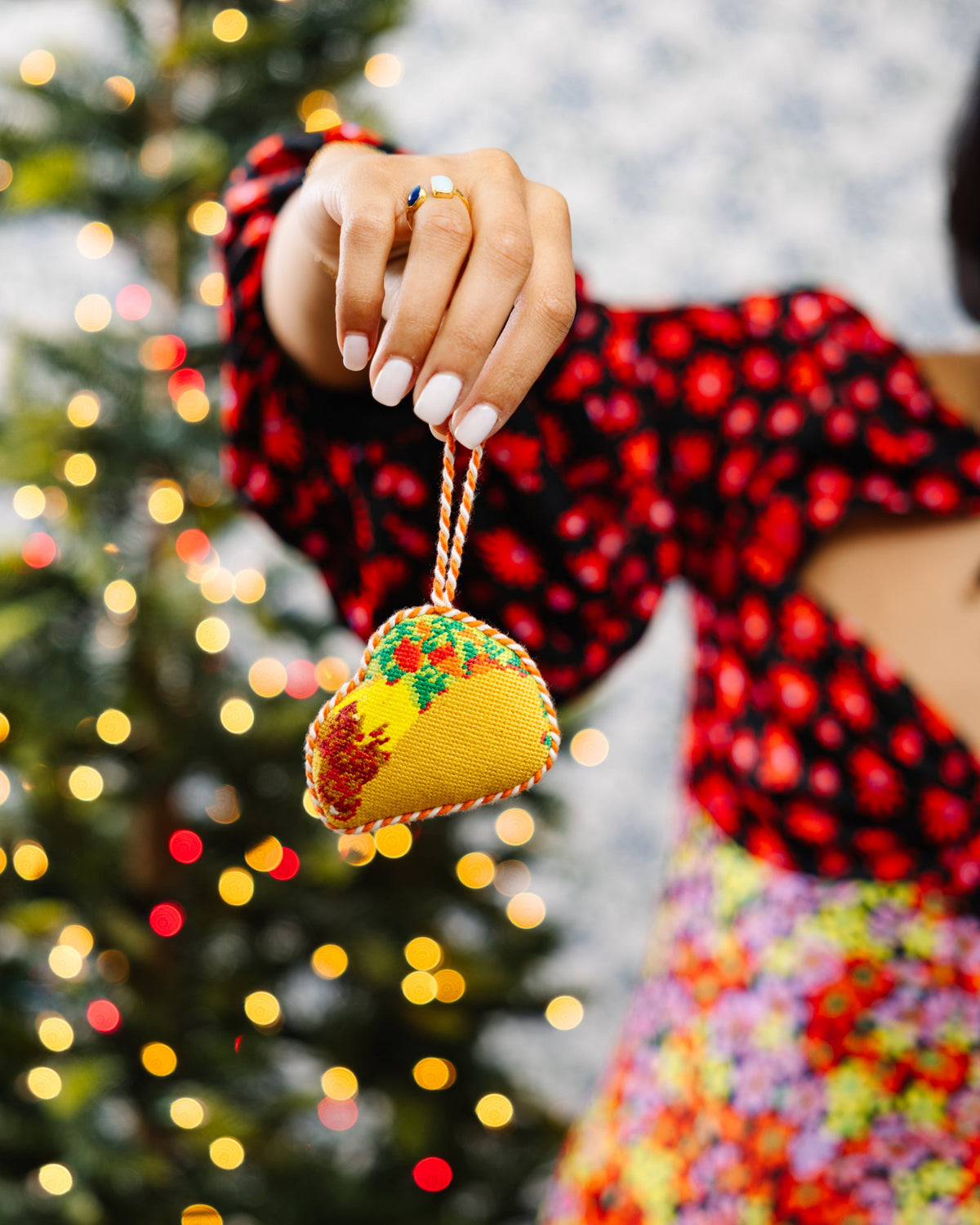 Person holding a festive taco ornament in front of a decorated Christmas tree.