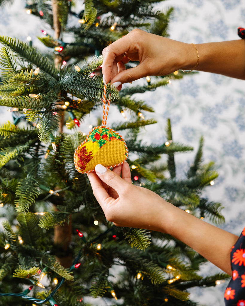 Person decorating a Christmas tree with a taco-shaped ornament.