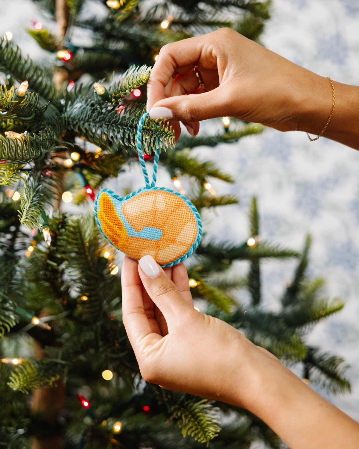 Hand holding a Christmas ornament against a decorated tree with lights.