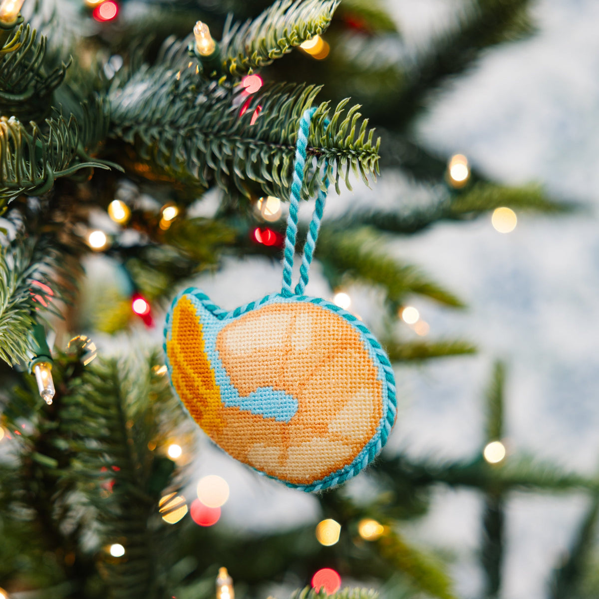Decorative ornament shaped like a world map hanging on a Christmas tree with lights.