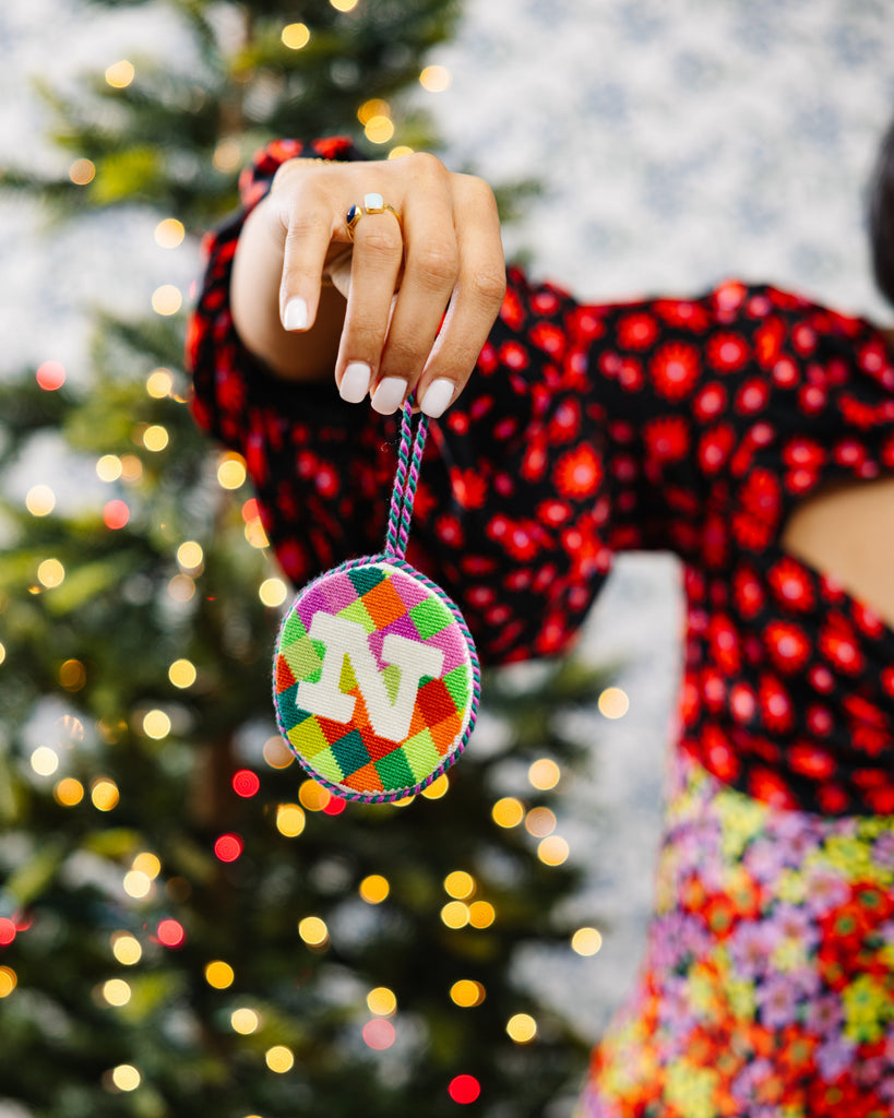 Colorful Christmas ornament held by a person in front of a decorated tree.
