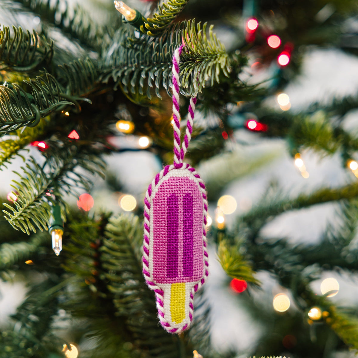 Decorative ice cream popsicle ornament on a Christmas tree with lights in the background
