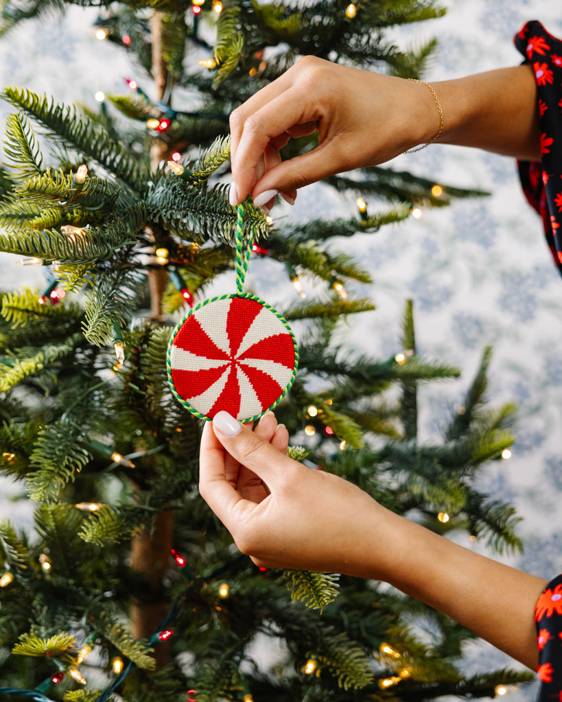 Person decorating a Christmas tree with a peppermint candy ornament.