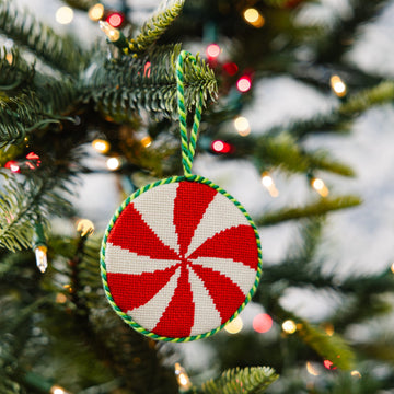 Red and white peppermint candy ornament on a Christmas tree with lights.