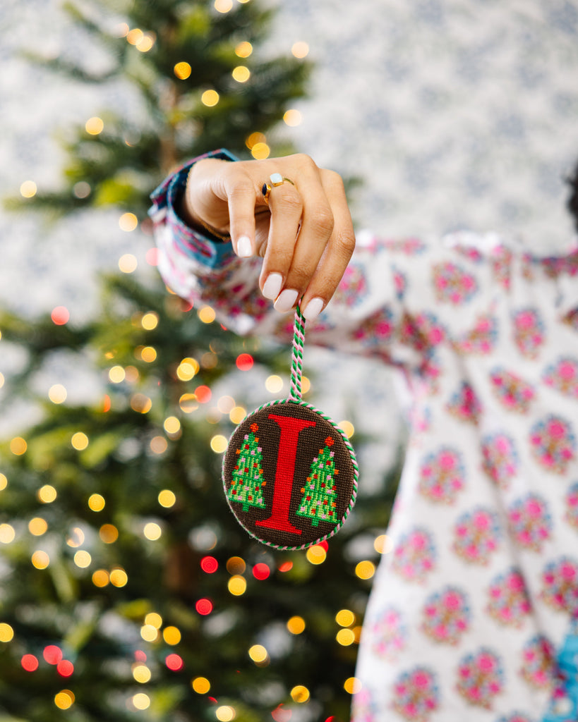 Person holding a Christmas ornament with a tree design in front of a decorated tree.