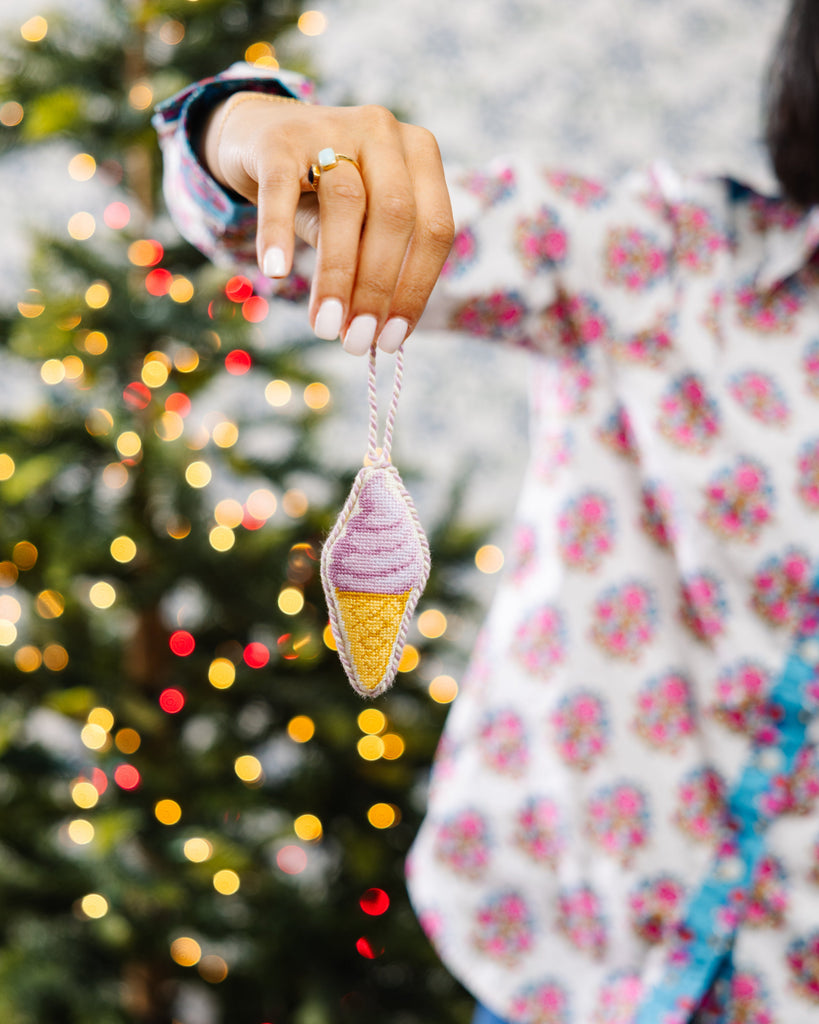 Person holding a colorful ice cream cone ornament in front of a decorated Christmas tree.