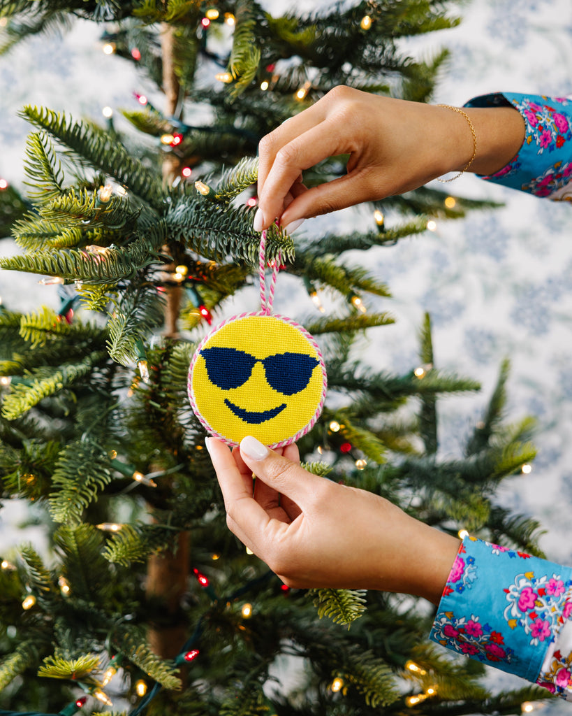Person decorating a Christmas tree with a smiley face ornament wearing sunglasses.