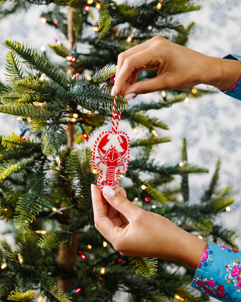 Person decorating a Christmas tree with a red and white ornament.