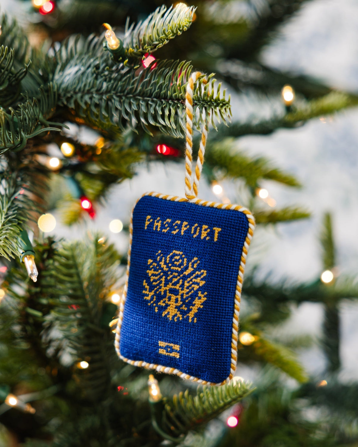 Blue passport ornament hanging on a decorated Christmas tree.