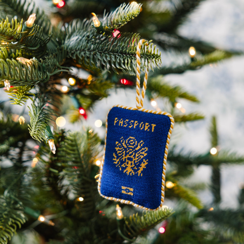 Blue passport ornament hanging on a decorated Christmas tree.
