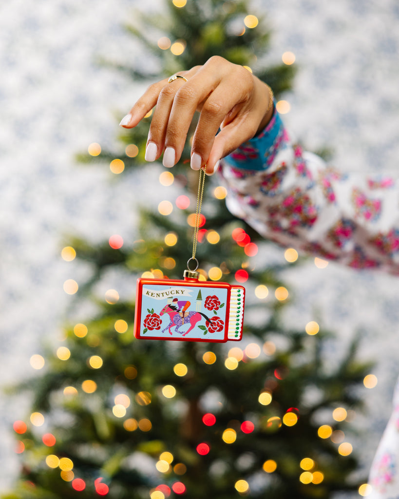 Hand holding a Christmas ornament with a tree in the background