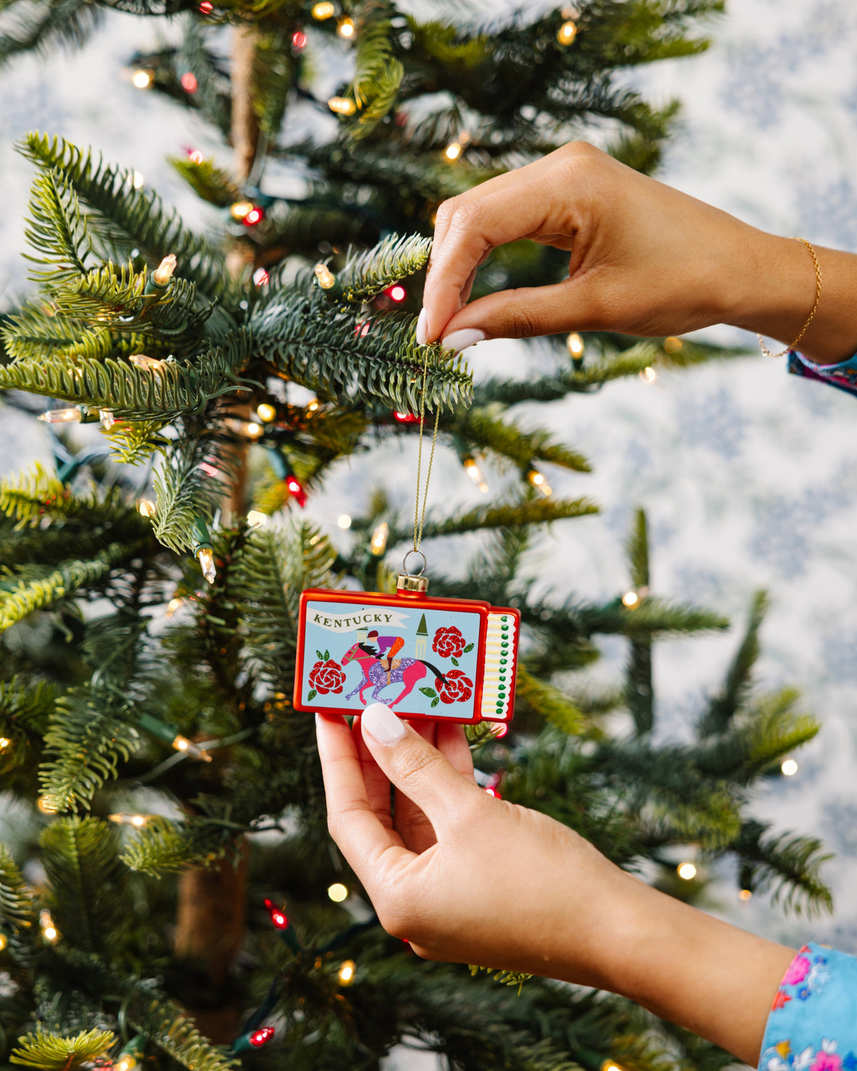 Person decorating a Christmas tree with a colorful ornament.