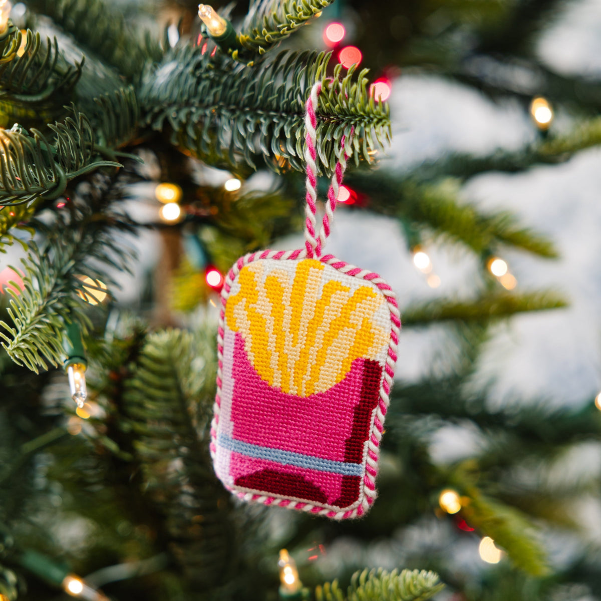 Decorative ornament shaped like a French fry on a Christmas tree with lights in the background