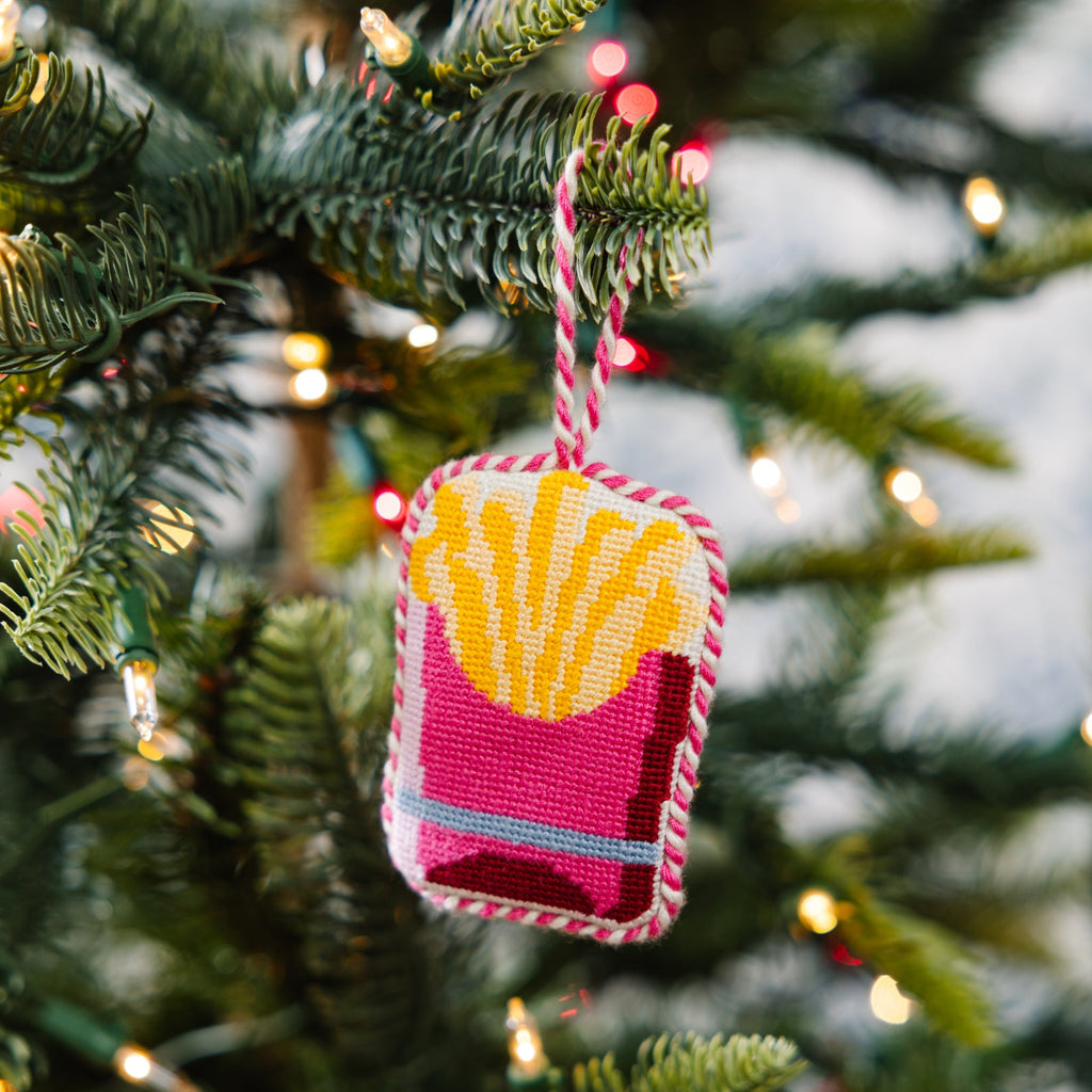 Decorative ornament shaped like a French fry on a Christmas tree with lights in the background