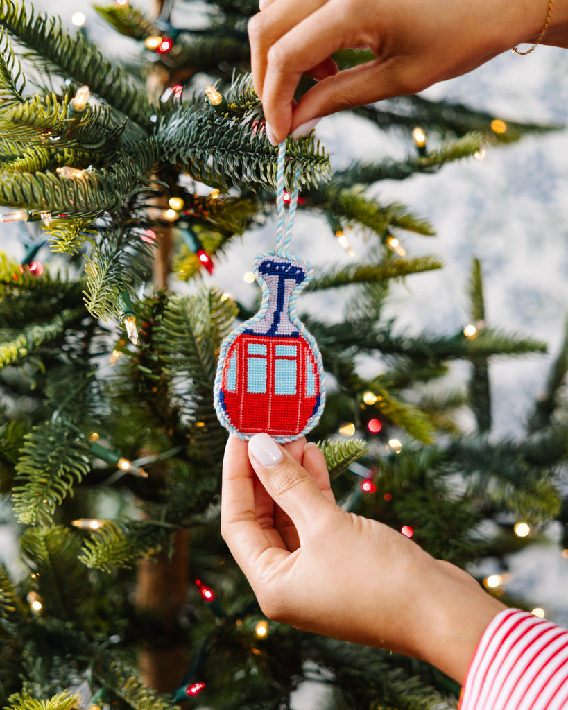 Person hanging a Christmas ornament shaped like a ski lift on a decorated tree.