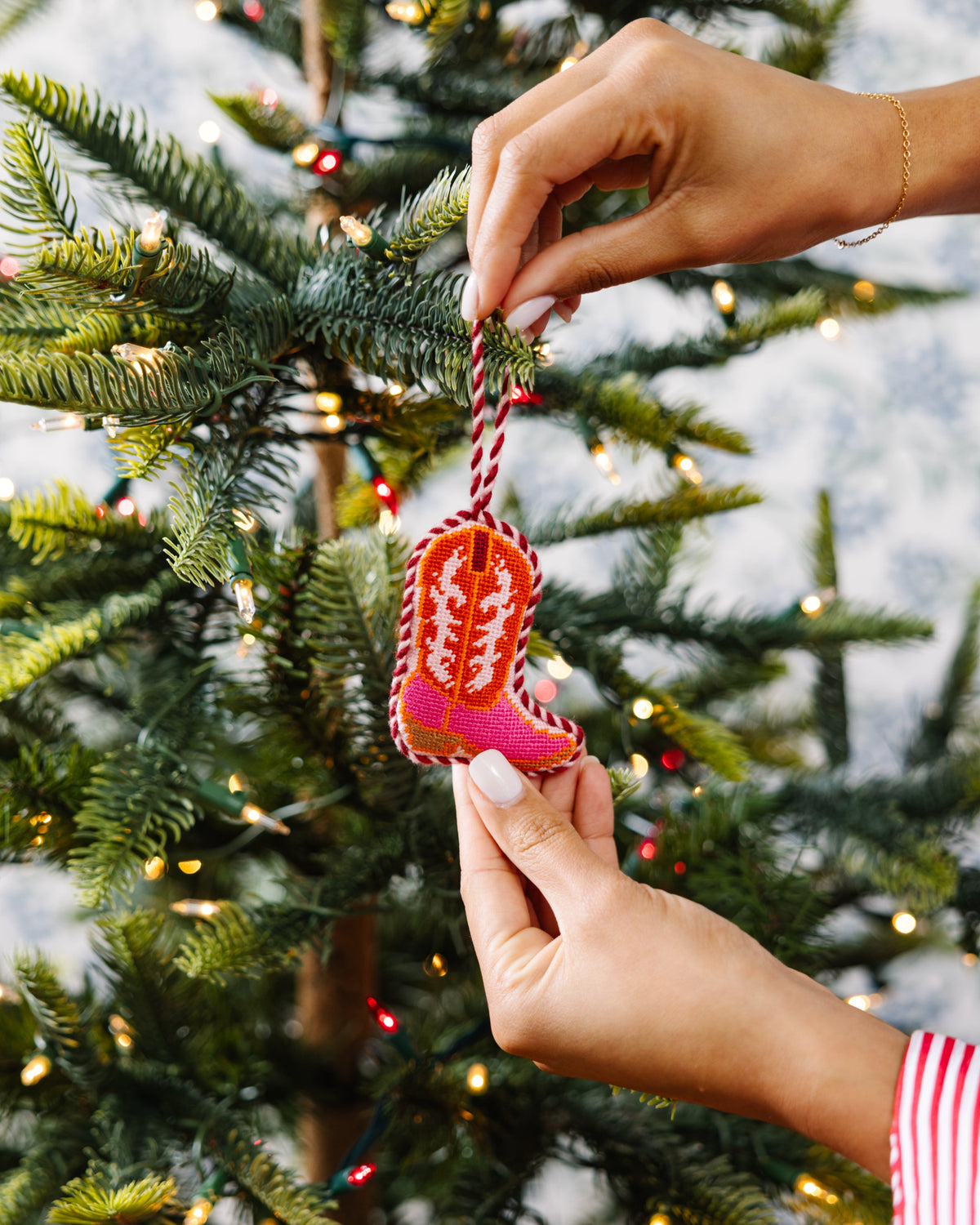 Hand placing a decorative boot ornament on a Christmas tree.