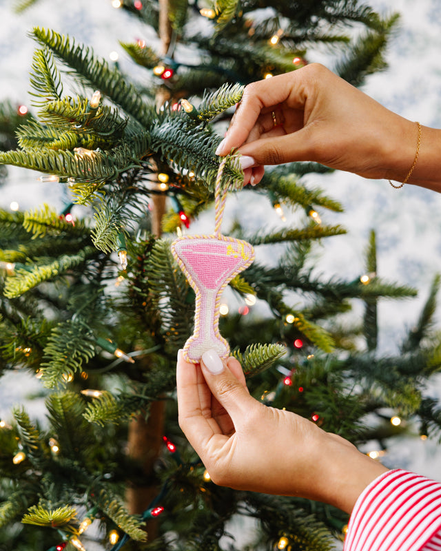Person decorating a Christmas tree with a pink ornament.
