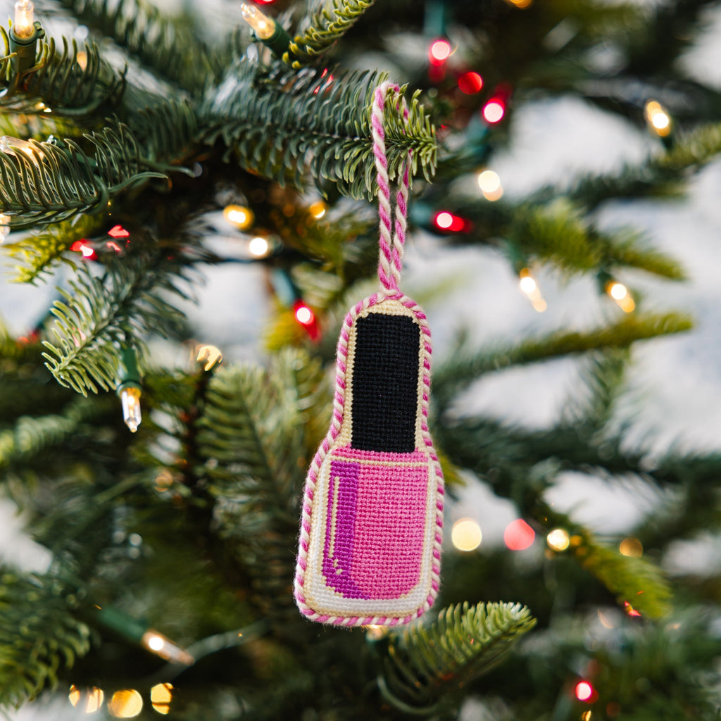 Pink nail polish bottle ornament hanging on a Christmas tree with lights.
