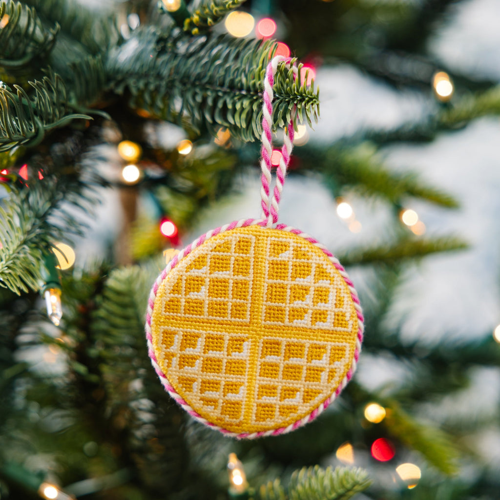 Decorative yellow waffle-patterned ornament on a Christmas tree with blurred lights in the background