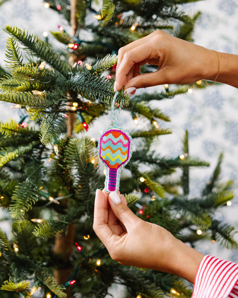 Person decorating a Christmas tree with a colorful ornament.