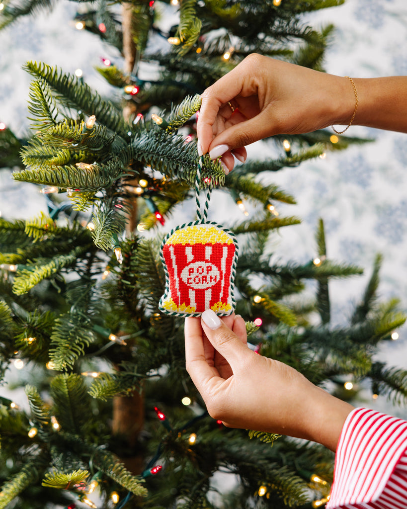 Hand holding a popcorn container ornament against a Christmas tree background