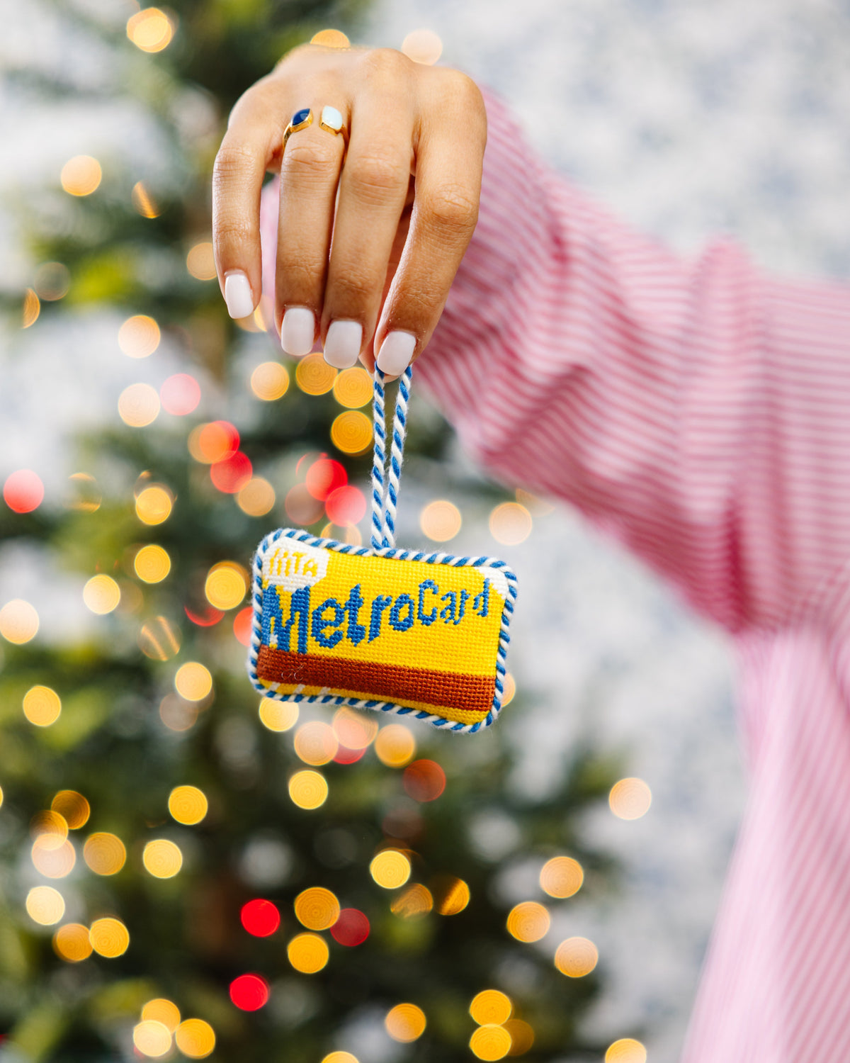 Decorative MetroCard ornament held in front of a Christmas tree with lights.