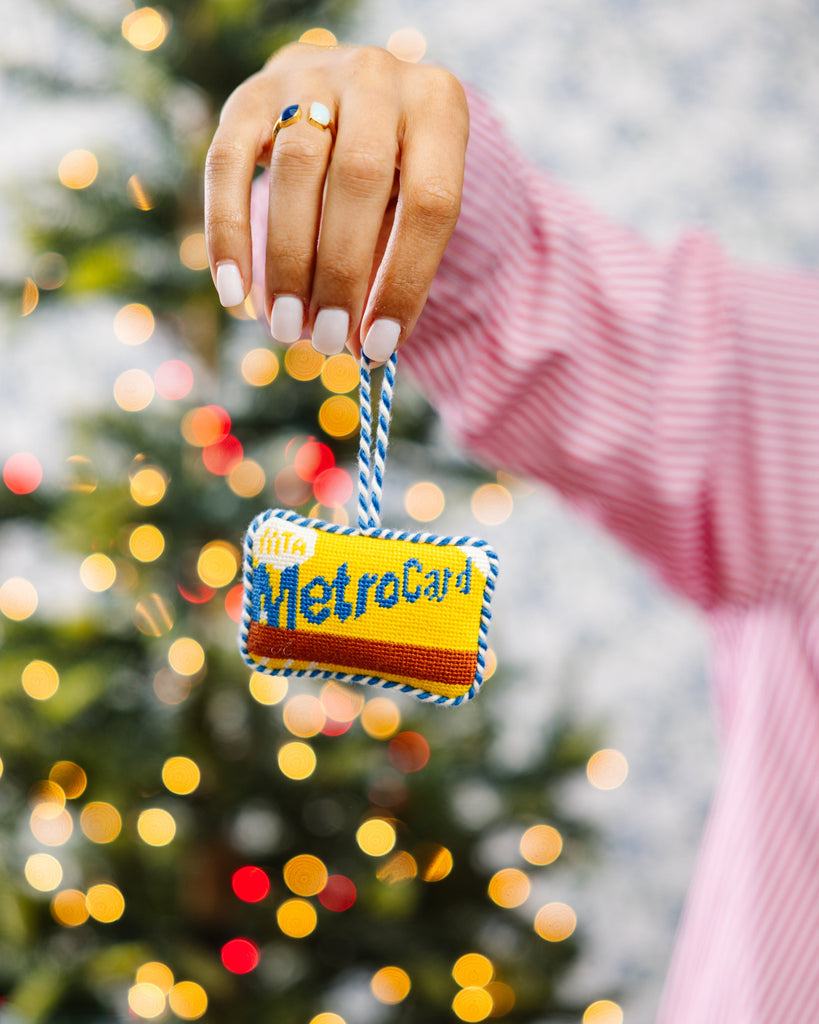 Decorative MetroCard ornament held in front of a Christmas tree with lights.