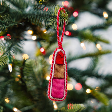 Decorative lipstick ornament on a Christmas tree with blurred lights in the background