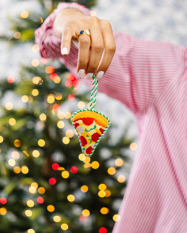 Hand holding a pizza-shaped ornament with a blurred Christmas tree in the background