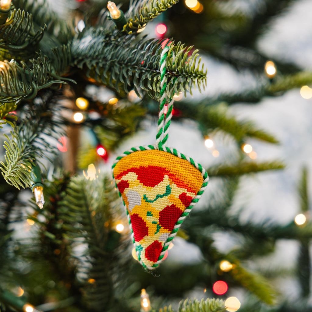 Decorative pizza ornament hanging on a Christmas tree with lights in the background