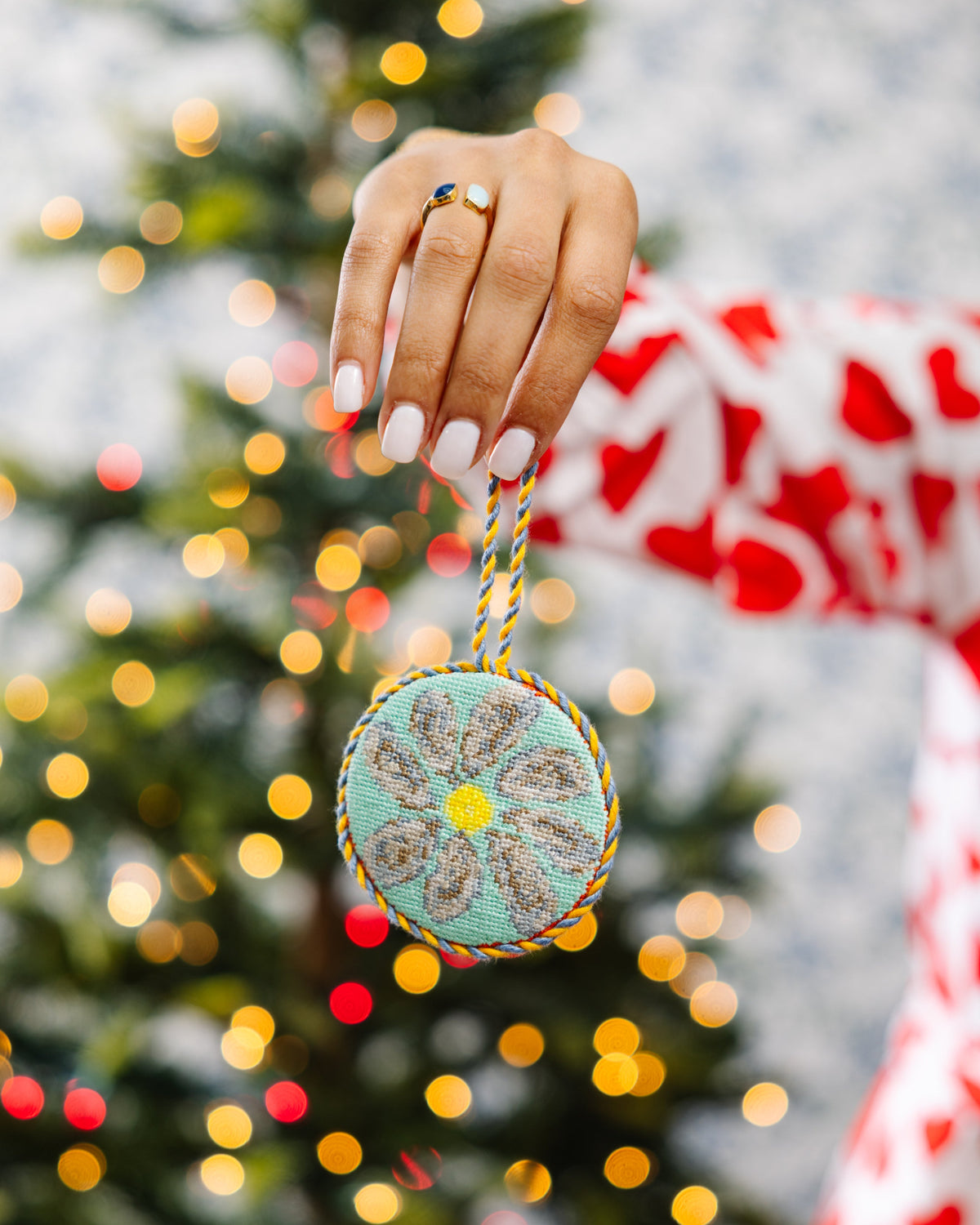 Hand holding a decorative ornament with a blurred Christmas tree in the background