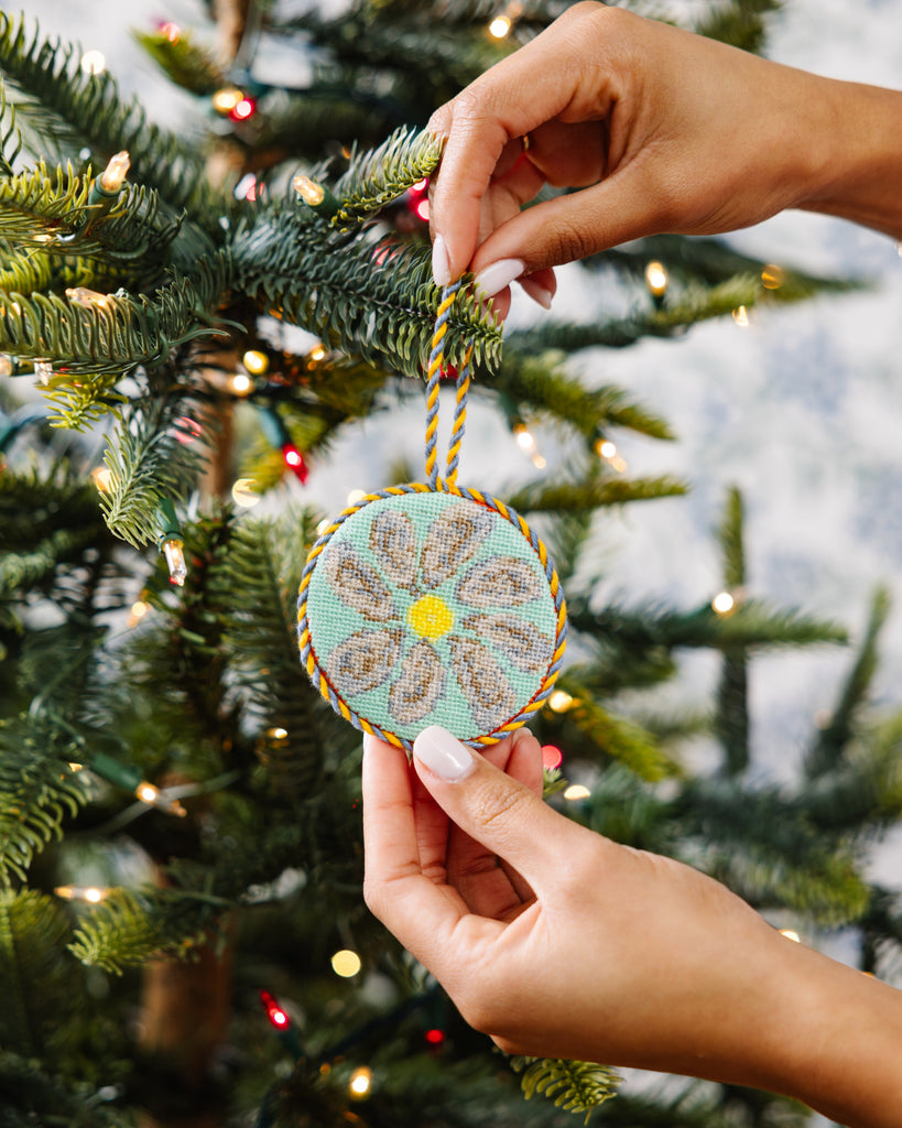 Hand holding a decorative ornament against a Christmas tree background