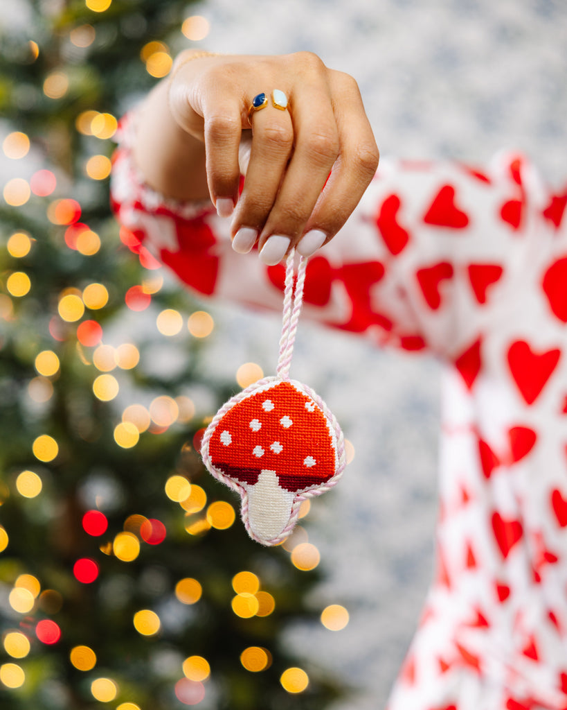 Hand holding a red and white mushroom ornament with a blurred Christmas tree in the background