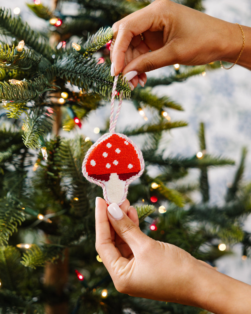 Hand holding a red and white mushroom ornament against a Christmas tree background