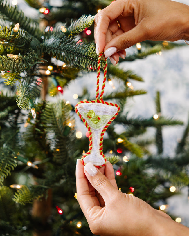 Hand holding a Christmas ornament shaped like a cocktail glass on a decorated tree.