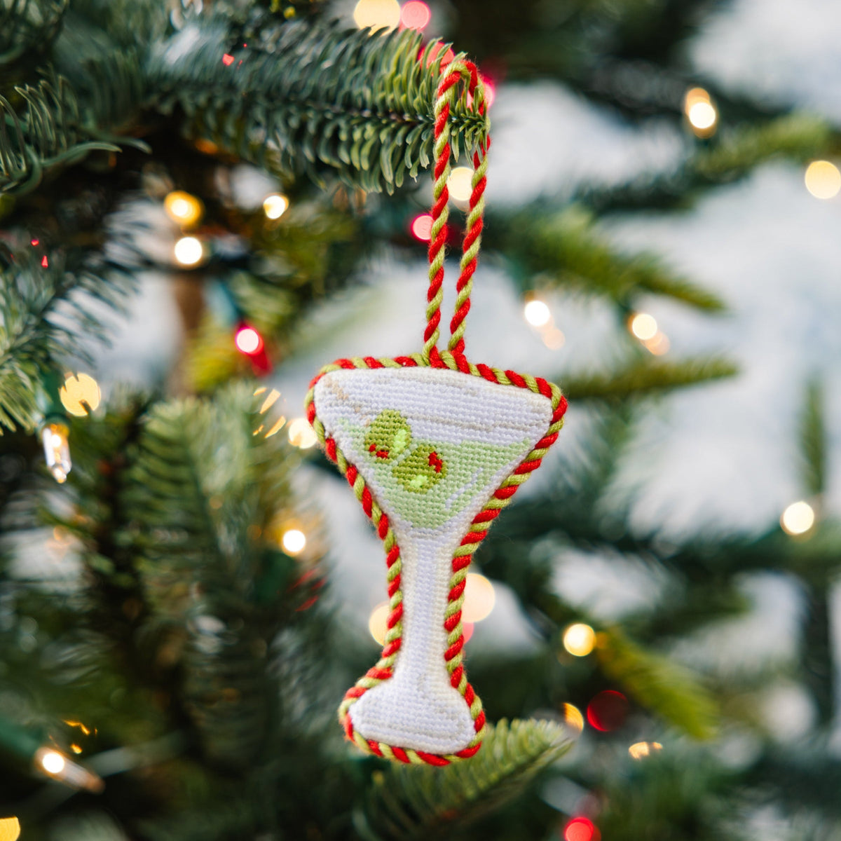 Decorative martini glass ornament on a Christmas tree with lights in the background