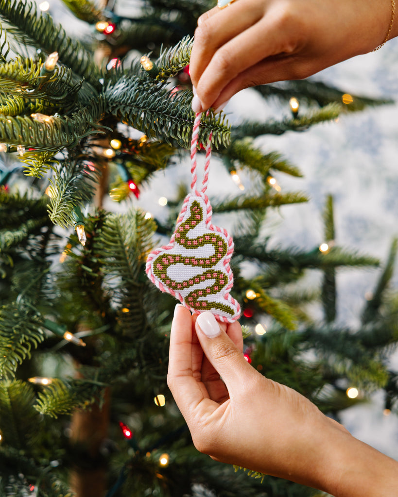 Hand holding a decorative ornament on a Christmas tree with blurred lights in the background