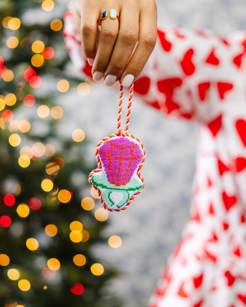Hand holding a colorful ornament with a blurred Christmas tree in the background
