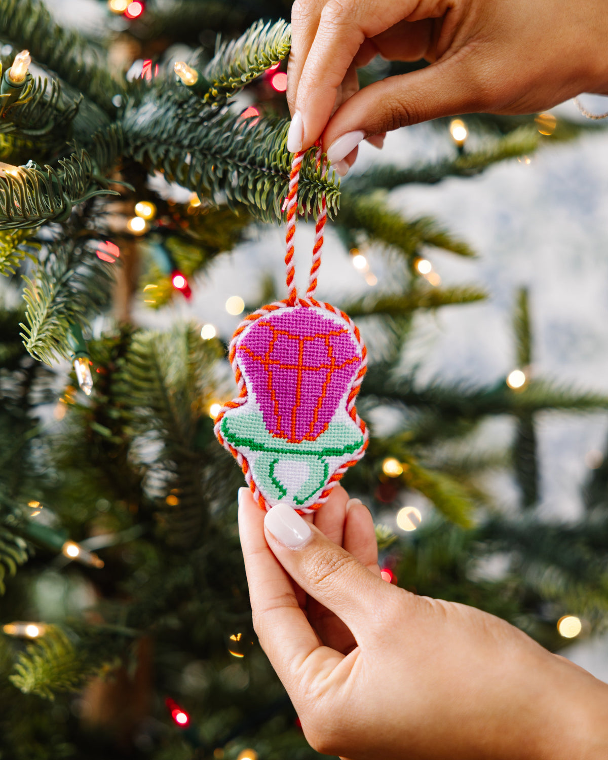 Hand holding a colorful embroidered ornament against a Christmas tree background