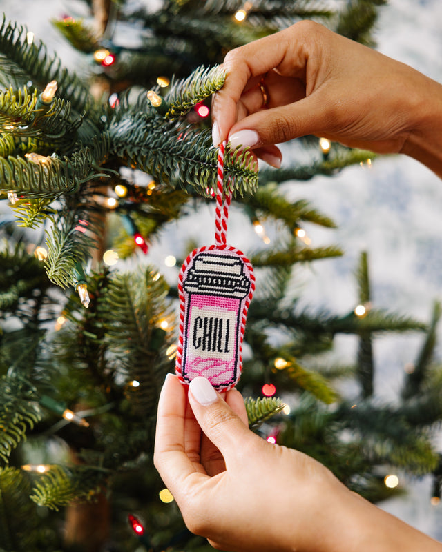 Hand holding a Christmas ornament with 'Chill' text in front of a decorated tree.